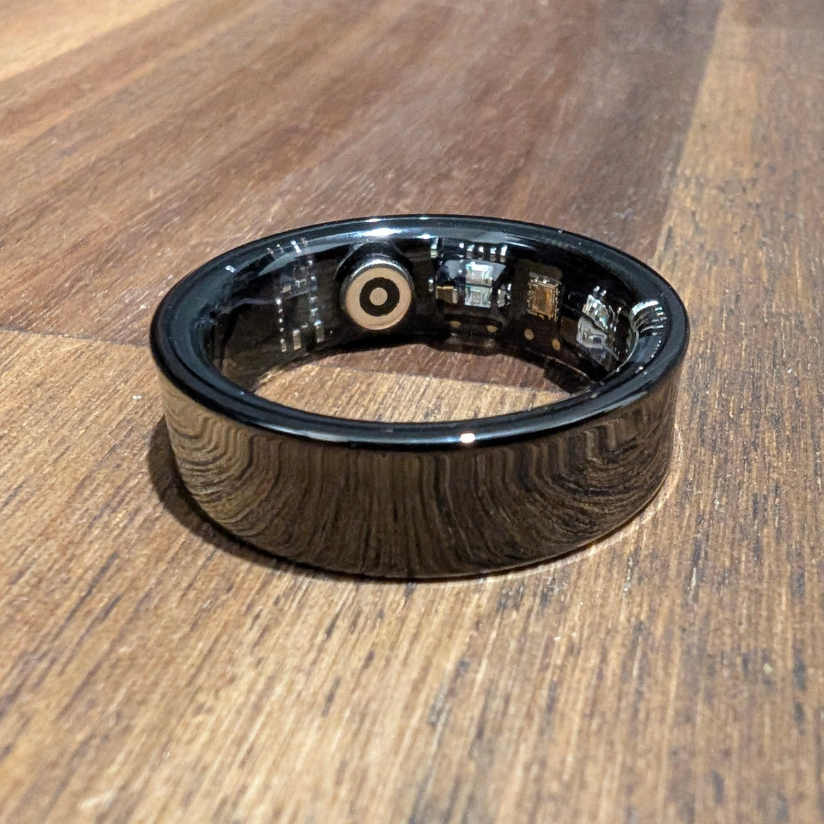 Black Quantum Ring smart ring on a wooden table, showing the sensors inside the band