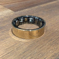 Gold Quantum Ring smart ring on a wooden table, showing the sensors inside the band