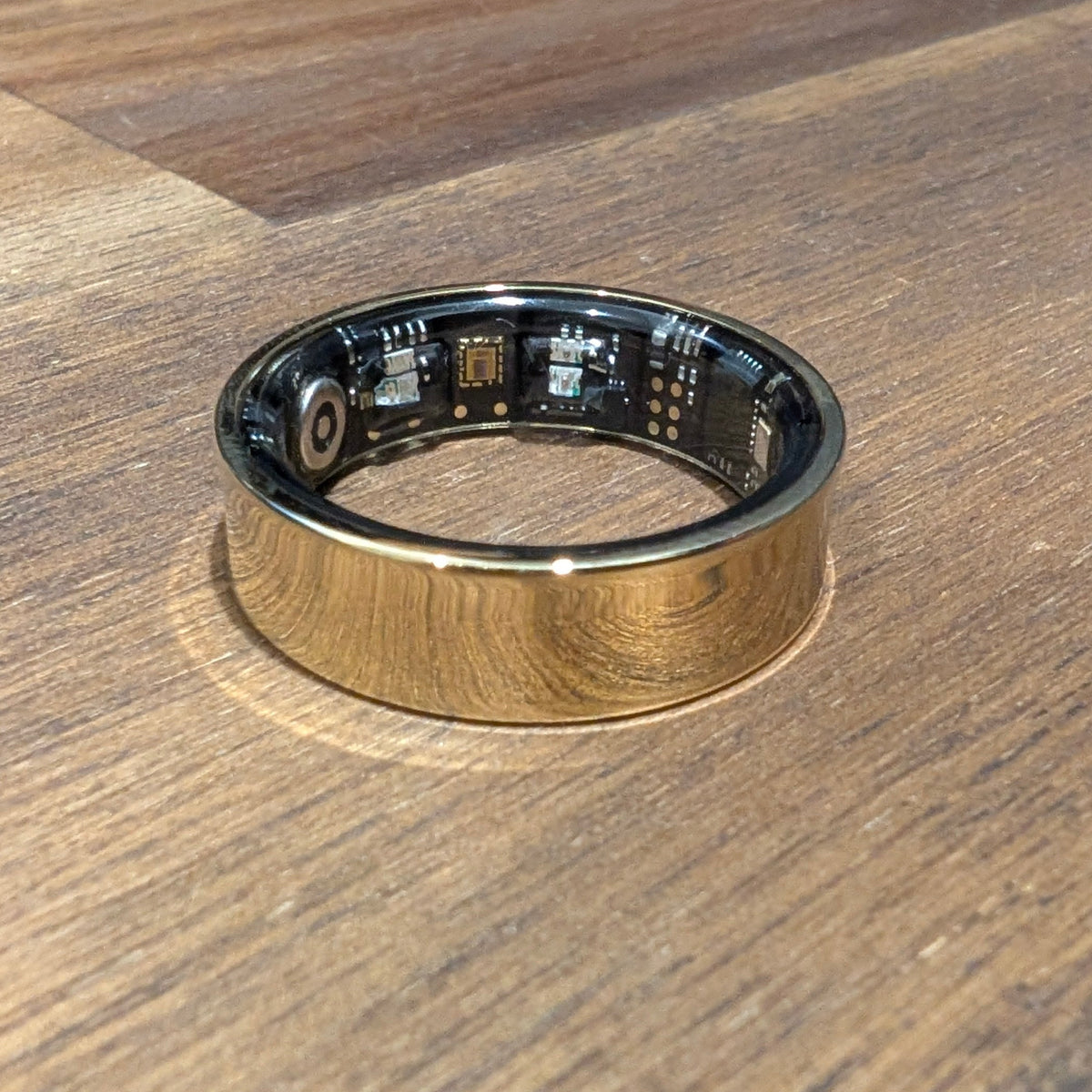 Gold Quantum Ring smart ring on a wooden table, showing the sensors inside the band
