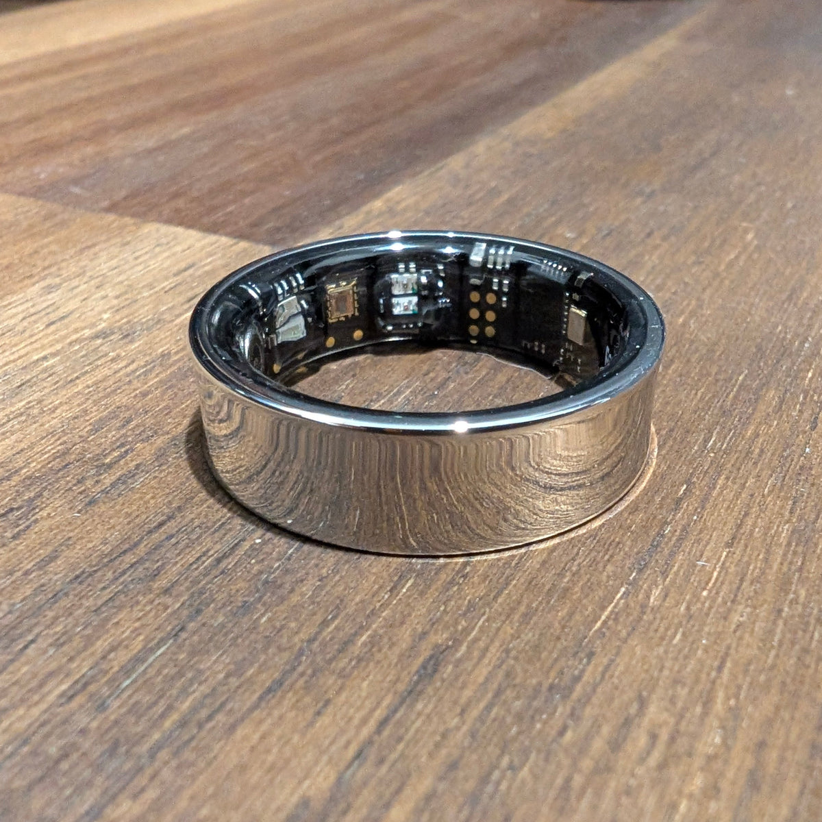 Silver Quantum Ring smart ring on a wooden table, showing the sensors inside the band
